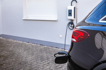 Generic electric vehicle EV hybrid car is being charged from a wallbox on a contemporary modern...
