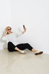 Funny woman sits on a floor and making selfie with smartphone