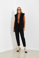 Stylish woman in chic black vest, terracotta sweater and tailored trousers, standing against a...