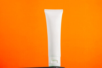 Plastic white tube for cream or lotion. Skin care or sunscreen cosmetic with stylish props on orange background 