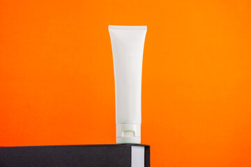 Plastic white tube for cream or lotion. Skin care or sunscreen cosmetic with stylish props on orange background 