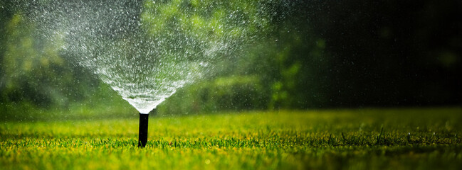Sprinkler system watering a lush green lawn on a sunny day. Wide shot