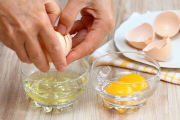 Woman hands breaking an egg to separate  egg white and  yolk. Egg shells on white plate at the background.