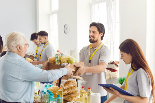 Poor people getting food aid at a charity center. Helpful volunteers give a senior man a box with pasta, oil, canned food and other stuff. Donation, poverty, help concept