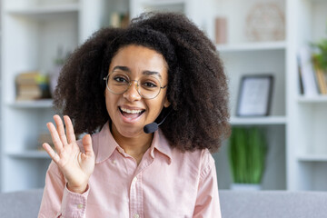 Happy customer service representative wearing a headset, waving and engaging in a video call from...