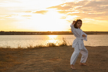 Cute little girl in kimono practicing karate near river at sunset