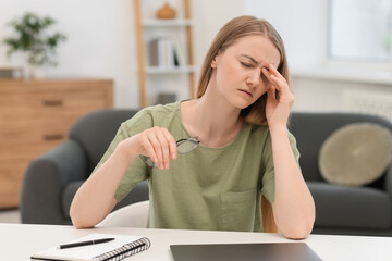 Overwhelmed young woman sitting with laptop at table in room