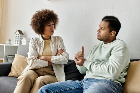 An African American couple uses sign language to communicate while sitting on a couch.
