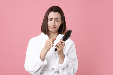 Sad woman holding brush with lost hair on pink background. Alopecia problem