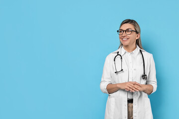 Portrait of happy doctor with stethoscope on light blue background, space for text
