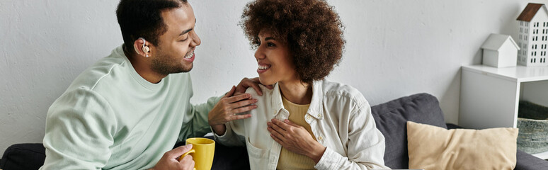An African American couple is sitting on a couch, using sign language to communicate with each other.