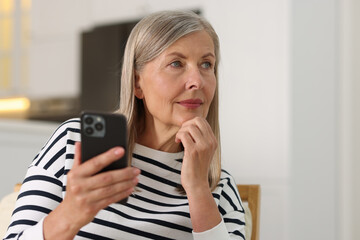 Senior woman using mobile phone at home, space for text