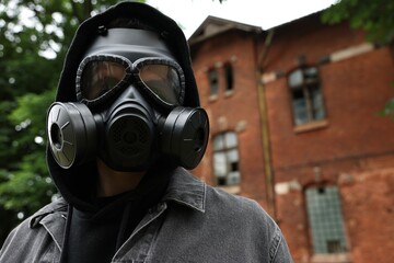 Man in gas mask near building outdoors, low angle view. Space for text