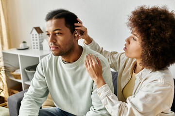 An African American woman helping her husband with hearing aid while at home.