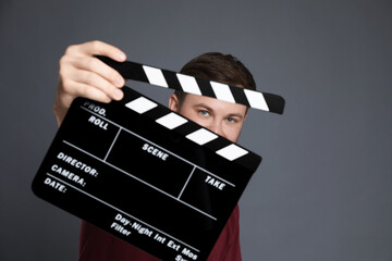 Making movie. Man with clapperboard on grey background