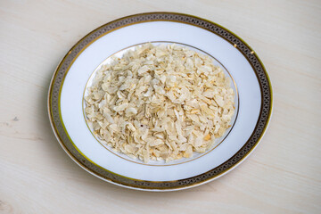 Flattened rice on a white plate on wooden background. It is also known as chiwda, chira, pohe, aval, pauwa, sira, chivda, or avalakki.