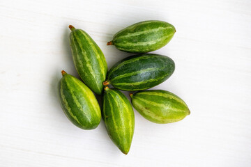 Fresh pointed gourd (Trichosanthes dioica) isolated on light wooden surface. It is also known as potol, parwal, palwal, or parmalin in different parts of Bangladesh and India. Top view.