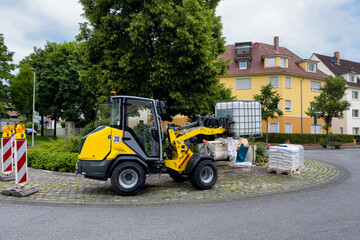 Yellow construction forklift holding a plastic container with water on a background of construction materials.