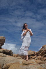 portrait of female model  standing wearing white goddess dress, dramatic natural landscape background of rocky ocean shoreline with stone clifftops. castle rock, Busselton, Western Australia