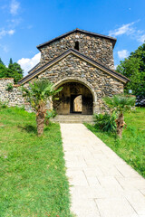 Arched stone entrance to the Ubisa monastery. Tiled path, palm trees, green lawn. Bright sky with clouds