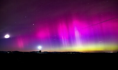 Aurora borealis illuminating field at night with moon and small dot