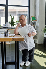 Fototapeta premium A man with inclusivity in a white shirt stands at a desk, reviewing documents in a bright office setting.