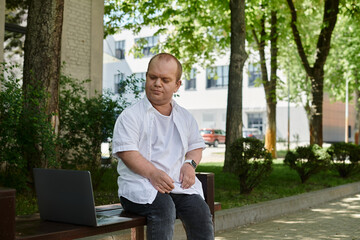 Obraz premium A man with inclusivity sits on a park bench, with a laptop beside him.
