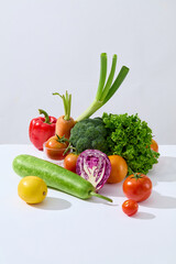 Many fresh vegetables are placed in a cluster on the white table, standing out against the gray background. All vegetables contain healthful vitamins, minerals, and dietary fiber