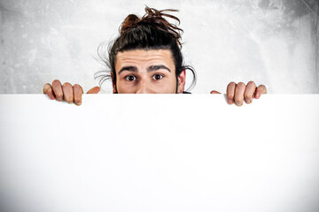 Astonished young man hiding behind a blank sign