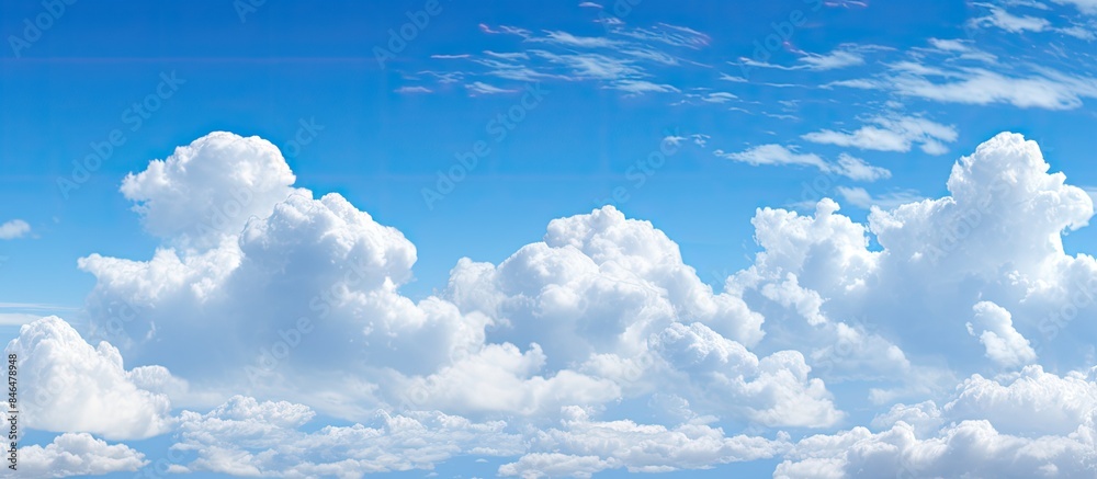 Poster Fluffy white clouds floating in a clear blue sky providing ample empty space for an image