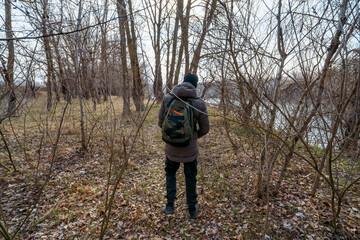 A teenage boy walking along the riverbank and forest, early spring landscape, the concept of hiking and outdoor activities