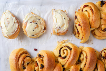 freshly baked cinnamon mixed fruit slice bun with cream cheese frosting on a baking paper.