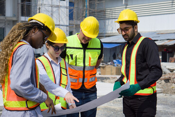 Group of construction workers gathered at a construction site reviewing some plan. Unfinished building, piles of construction material, and a partially constructed structure are in the background