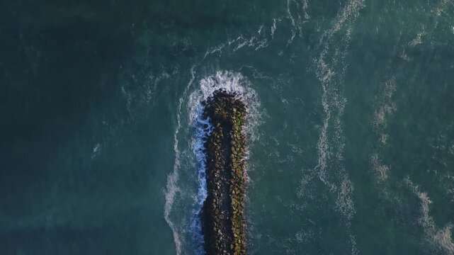 Slow motion drone footage of the ocean waves crashing on Espigon Waikiki stone pier in Lima, Peru