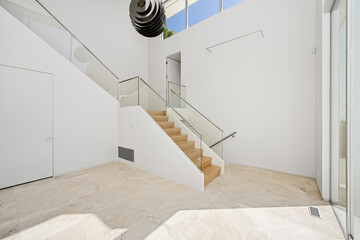 Interior of contemporary white house with curved glass railings and wooden staircase