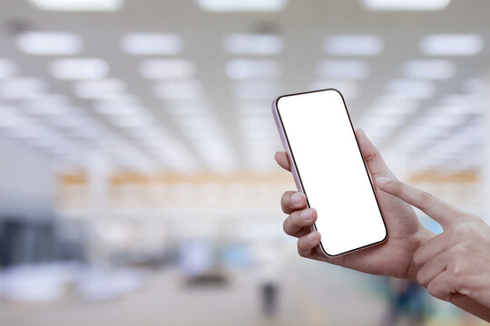 Close-up of a woman hand holding a smartphone white screen at factory background. Transparent mobile screen mockup.