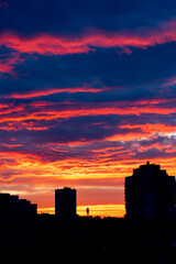 Orange-red colored cloudy sky after sunset, cloud formation, evening sky, sunset. City houses against the evening sky