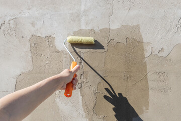 The girl's hand holds a roller dipped in primer and covers the front wall of the house with primer.