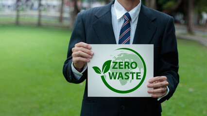 Businessman a suit is holding a sign that says "zero waste" with a green leaf and the outline of the earth on it. The picture is a call for environmental awareness and taking action to reduce waste.