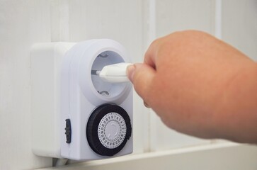 Naklejka premium A woman's hand connects a plug to a socket with a timer to save energy
