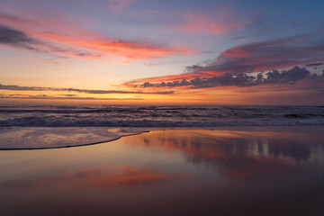 Sunset landscape of a beautiful and paradisaical beach with the clouds reflected on the water. Summer and vacations concept background.