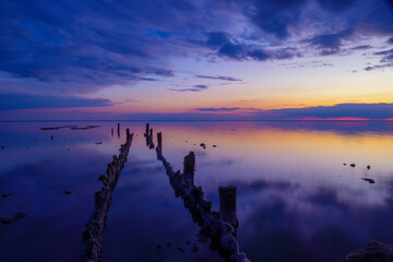 A tranquil sunset scene with vibrant colors reflecting on calm water, featuring old wooden posts. Perfect for peaceful, nature-oriented designs.