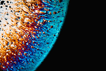 Close-up of a soap foam bubble with iridescent surface area on a black background