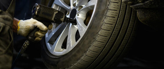 Repairman using pneumatic wrench while changing car wheel in garage, web banner