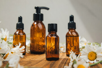 Set of natural cosmetics. Amber bottles with facial, bath liquid on a wooden table with white field chamomile. Front view