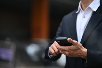 Cropped shot businessman in a suit using smartphone while standing outside the office