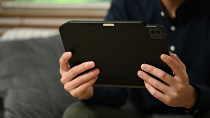 Young businessman reading email on digital tablet and relaxing on couch in living room