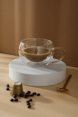 Golden coffee capsule, spoon and glass cup with coffee drink on beige background