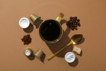 Coffee capsules and beans, sugar, cup with spoon on brown background, top view