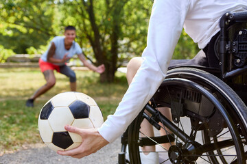 Person in wheelchair holding a soccer ball, playing with friend at the park